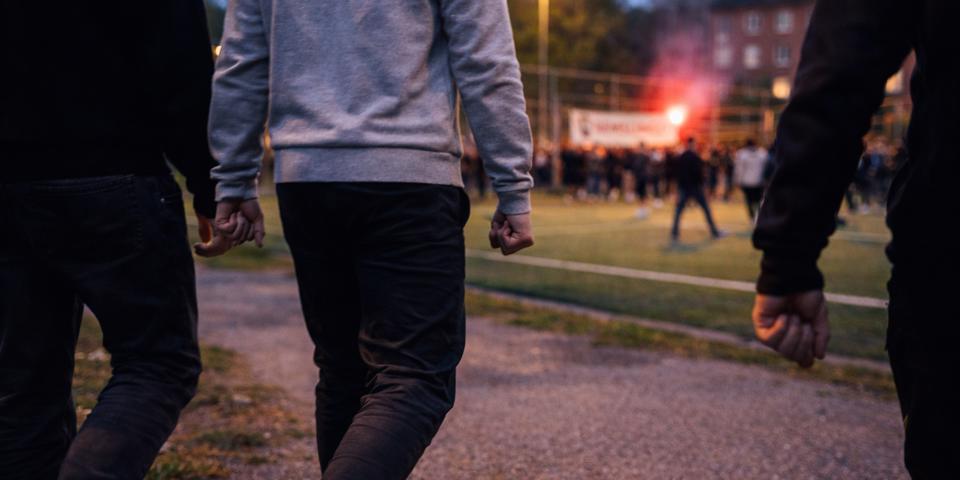 Tre personer går med knutna nävar mot en folksamling på en upplyst fotbollsplan.