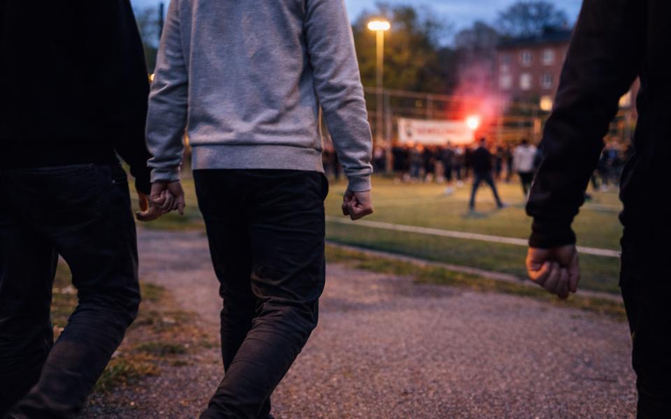 Tre personer går med knutna nävar mot en folksamling på en upplyst fotbollsplan.